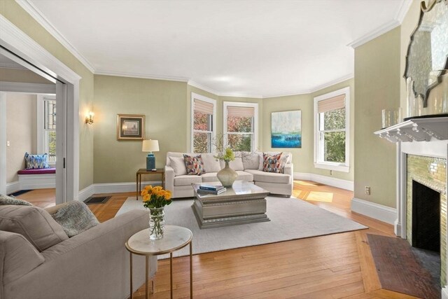 living area with crown molding, a premium fireplace, baseboards, wood finished floors, and visible vents