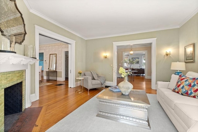 living area featuring a fireplace with flush hearth, baseboards, ornamental molding, and wood finished floors