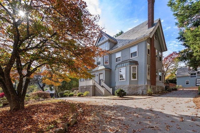 victorian-style house featuring a chimney, roof with shingles, and stone siding