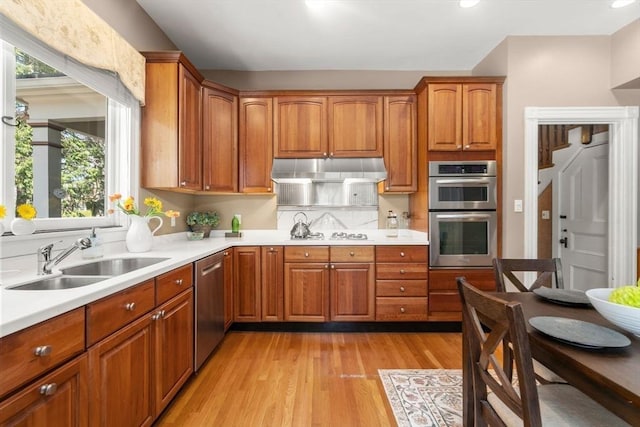 kitchen with under cabinet range hood, appliances with stainless steel finishes, a sink, and light countertops