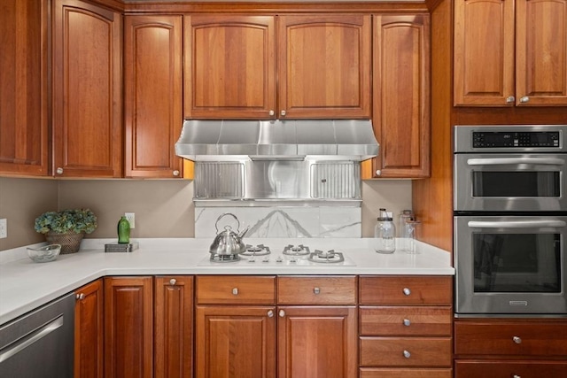 kitchen with light countertops, brown cabinetry, stainless steel appliances, tasteful backsplash, and under cabinet range hood