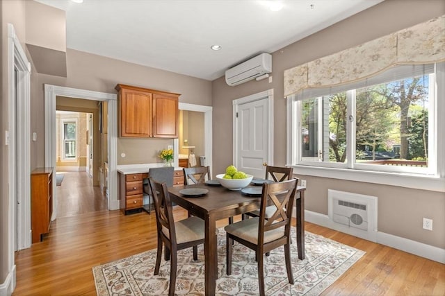 dining room with baseboards, a wall mounted AC, light wood-type flooring, and a wealth of natural light