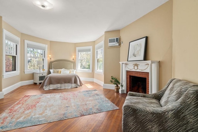 bedroom featuring baseboards, a wall mounted air conditioner, a brick fireplace, and wood finished floors
