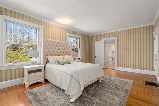 bedroom featuring visible vents, crown molding, baseboards, wood-type flooring, and wallpapered walls
