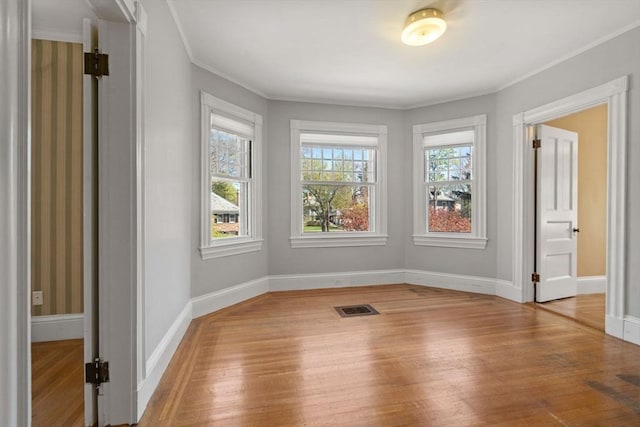 unfurnished room featuring baseboards, visible vents, ornamental molding, and wood finished floors
