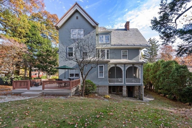 back of property featuring a chimney, a yard, a deck, and stone siding
