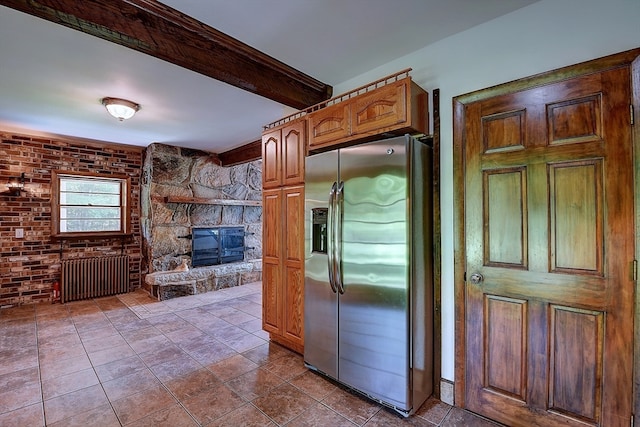 interior space with radiator, a fireplace, beamed ceiling, stainless steel fridge with ice dispenser, and brick wall