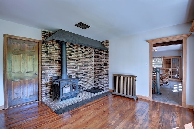 unfurnished living room featuring a wood stove, dark hardwood / wood-style flooring, and radiator heating unit