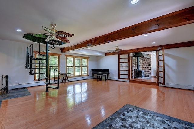 unfurnished living room featuring ceiling fan, baseboard heating, beam ceiling, hardwood / wood-style floors, and a wood stove