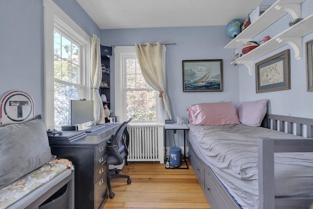 bedroom featuring light wood-style floors, multiple windows, and radiator