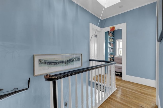 hallway featuring a skylight, wood finished floors, crown molding, and baseboards