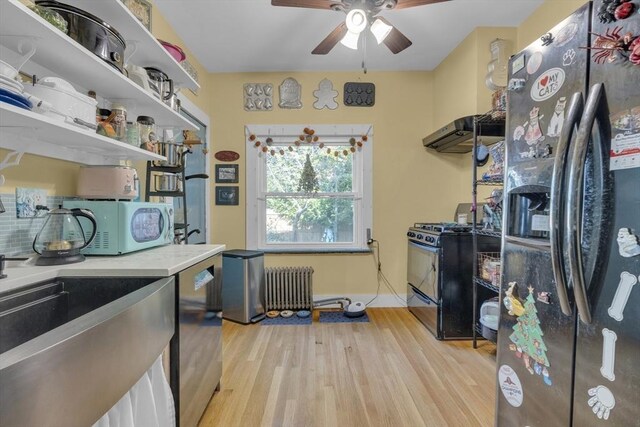 interior space with ceiling fan, white microwave, radiator, refrigerator with ice dispenser, and gas range oven