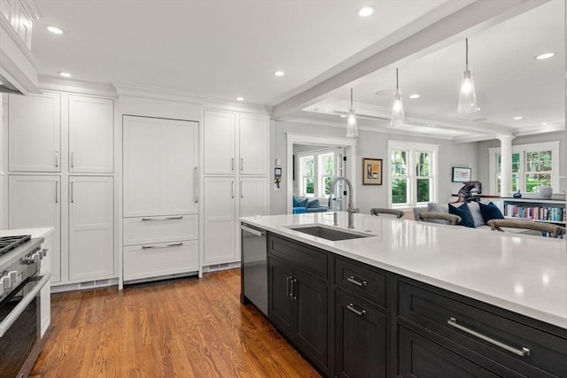 kitchen featuring stainless steel dishwasher, a sink, dark cabinets, ornate columns, and white cabinetry