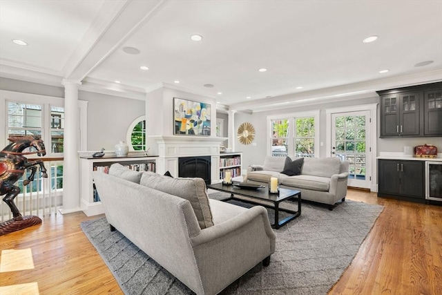 living room featuring a fireplace, light wood-style floors, recessed lighting, ornamental molding, and a bar