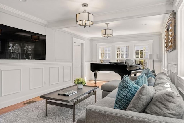 living room featuring crown molding, a decorative wall, wood finished floors, and visible vents