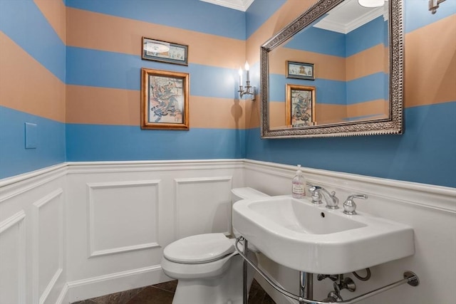 bathroom with a decorative wall, ornamental molding, wainscoting, and toilet