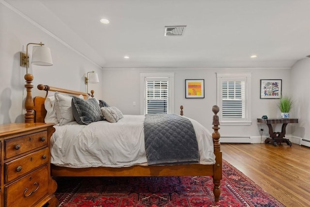 bedroom featuring visible vents, a baseboard radiator, wood finished floors, and multiple windows