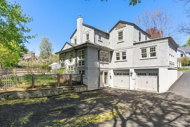 exterior space with a garage, fence, stucco siding, a chimney, and driveway