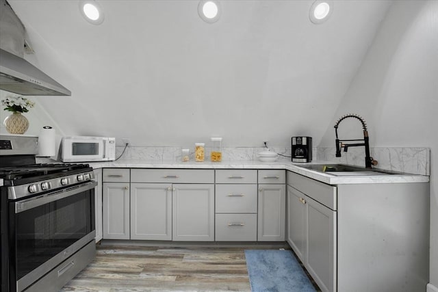 kitchen featuring stainless steel range with gas stovetop, white microwave, wall chimney range hood, a sink, and gray cabinetry