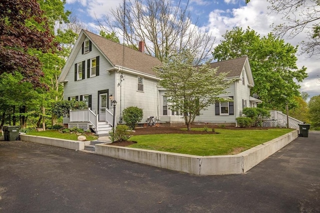 view of front of house with a chimney, a shingled roof, and a front lawn
