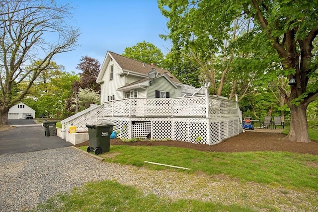 view of side of home with an outdoor structure, a deck, a lawn, and view of scattered trees