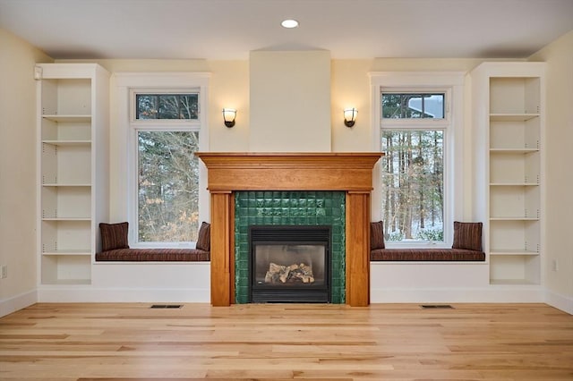 unfurnished room featuring a tiled fireplace, wood-type flooring, and built in shelves