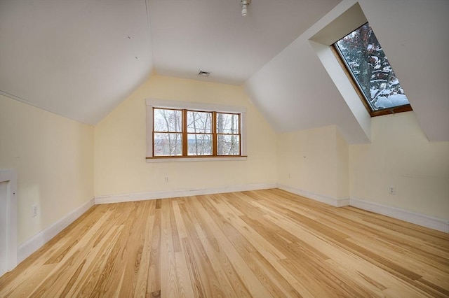 additional living space with vaulted ceiling with skylight and light wood-type flooring