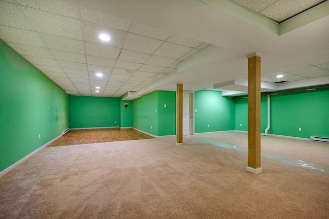 basement with a baseboard heating unit, carpet floors, and a drop ceiling