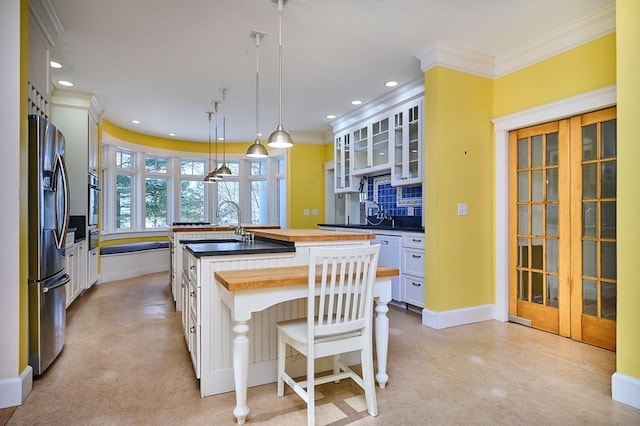 kitchen with wood counters, hanging light fixtures, appliances with stainless steel finishes, an island with sink, and white cabinets