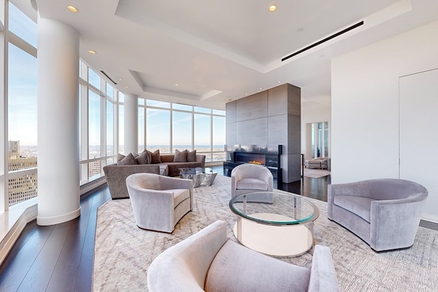 living room featuring a raised ceiling, a healthy amount of sunlight, wood-type flooring, and expansive windows