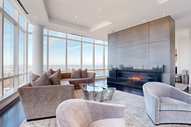 living room featuring floor to ceiling windows, a water view, light hardwood / wood-style flooring, a fireplace, and a tray ceiling