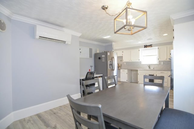 dining room with crown molding, light wood finished floors, a chandelier, a wall mounted air conditioner, and baseboards