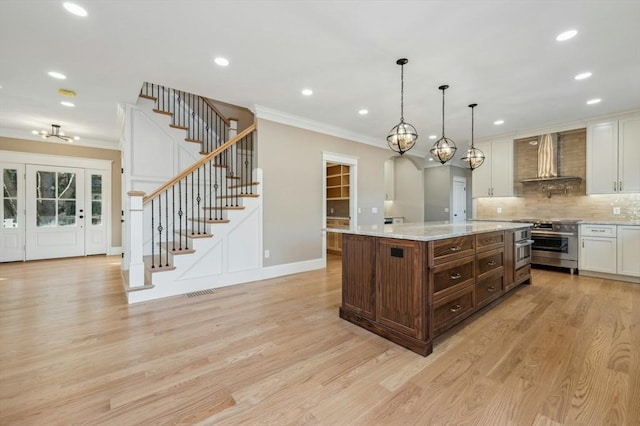 kitchen featuring stainless steel range, wall chimney range hood, decorative light fixtures, white cabinets, and a kitchen island