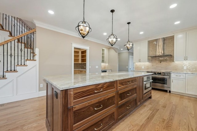 kitchen with a center island, white cabinets, wall chimney range hood, hanging light fixtures, and appliances with stainless steel finishes