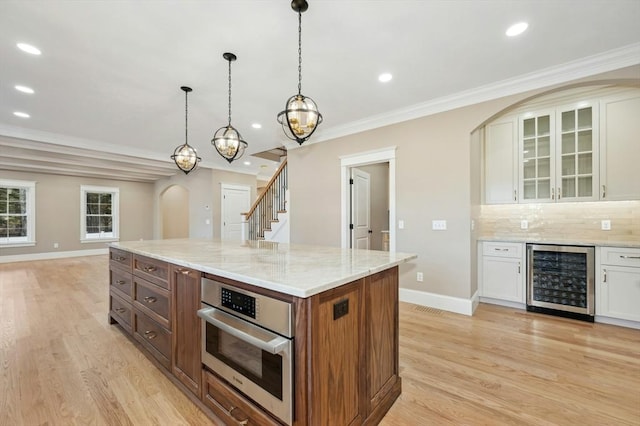 kitchen featuring backsplash, stainless steel oven, beverage cooler, white cabinets, and a kitchen island