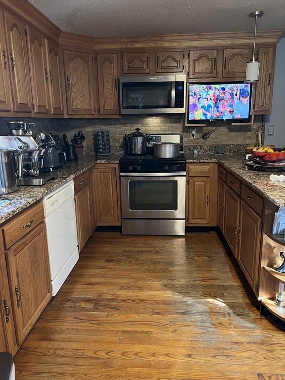 kitchen with dark hardwood / wood-style floors, backsplash, dark stone counters, decorative light fixtures, and appliances with stainless steel finishes