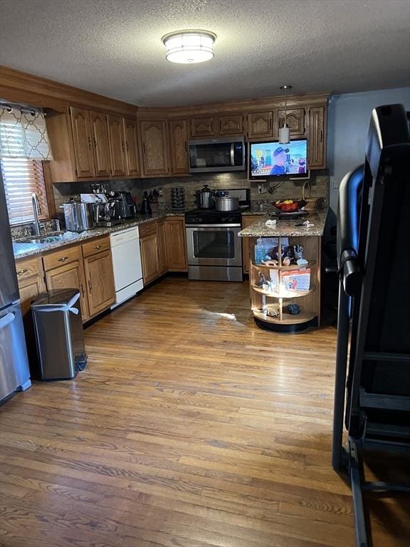 kitchen with light stone countertops, a textured ceiling, stainless steel appliances, sink, and hardwood / wood-style floors