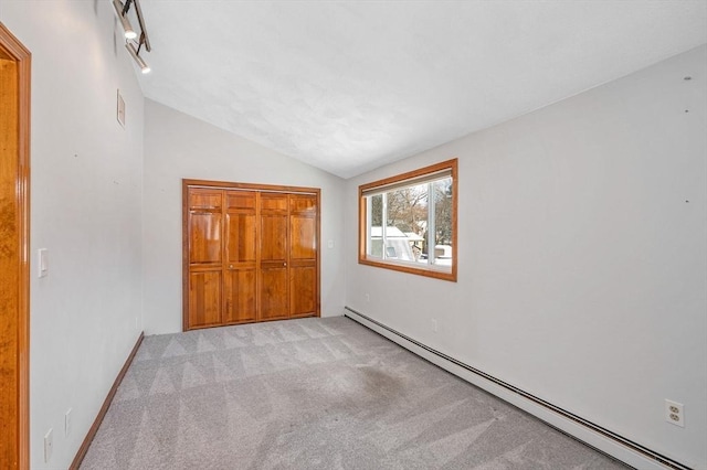 unfurnished bedroom with baseboard heating, light colored carpet, vaulted ceiling, and a closet