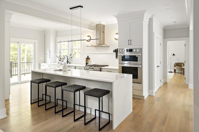 54 Stone Rd, Sudbury, MA 01776 - kitchen with stainless steel double oven, wall chimney range hood, a breakfast bar, light wood-style flooring, and a center island