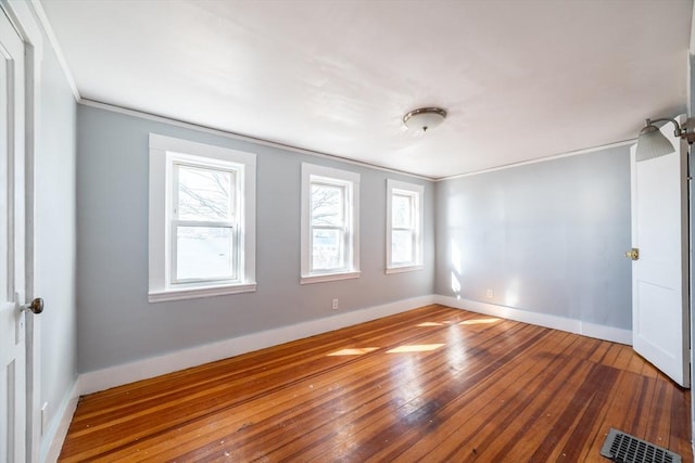 empty room featuring ornamental molding, visible vents, baseboards, and hardwood / wood-style flooring