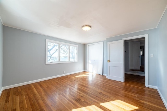 unfurnished bedroom featuring crown molding, a closet, wood finished floors, and baseboards