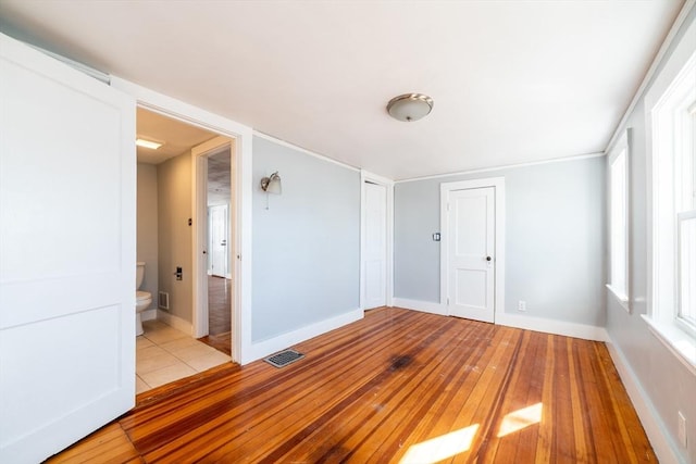 spare room featuring wood-type flooring, visible vents, and baseboards