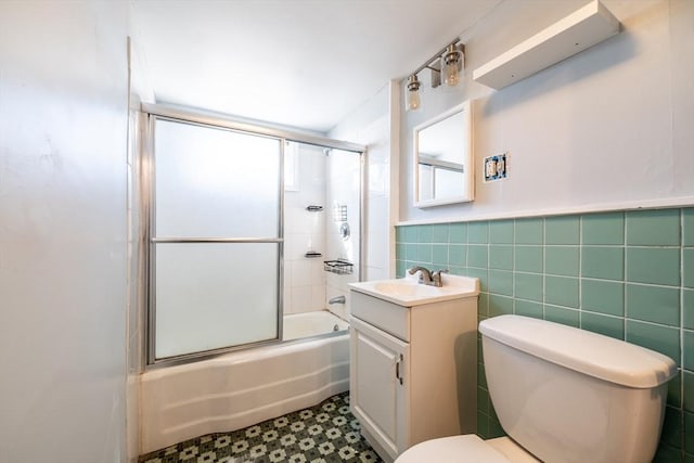 full bath with toilet, tile patterned floors, combined bath / shower with glass door, vanity, and tile walls