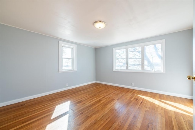 spare room featuring a healthy amount of sunlight, wood-type flooring, baseboards, and crown molding