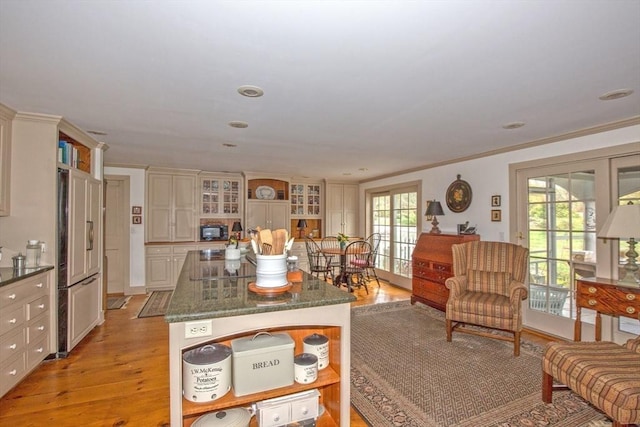 kitchen with crown molding, a center island, paneled built in refrigerator, glass insert cabinets, and light wood-style flooring