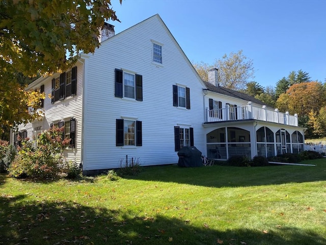 rear view of property featuring a lawn, a sunroom, a balcony, and a chimney