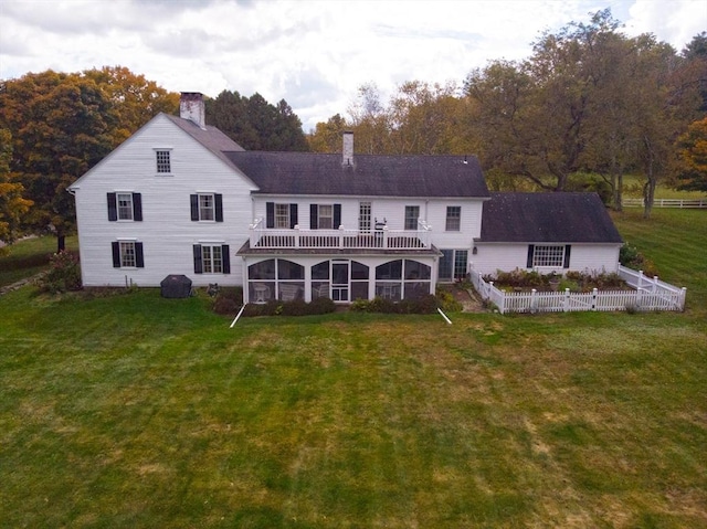 rear view of house featuring a lawn, a sunroom, a balcony, and a chimney
