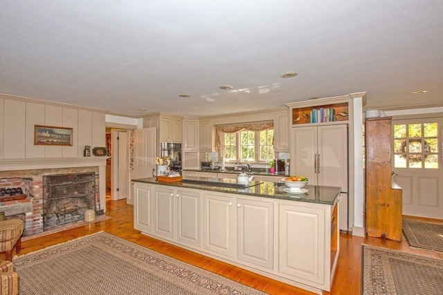 kitchen with dobule oven black, a kitchen island, a fireplace with flush hearth, dark stone countertops, and light wood-style flooring
