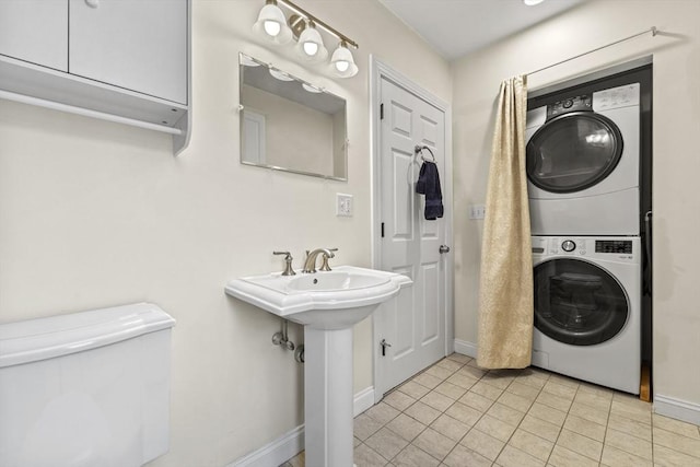 interior space featuring baseboards, a sink, tile patterned flooring, stacked washer / dryer, and toilet