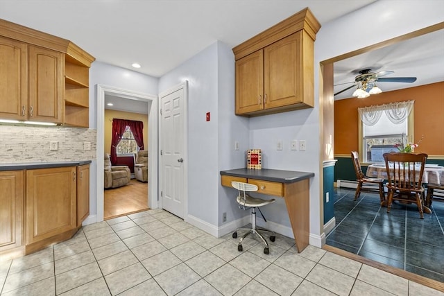 kitchen featuring brown cabinetry, light tile patterned flooring, ceiling fan, dark countertops, and backsplash